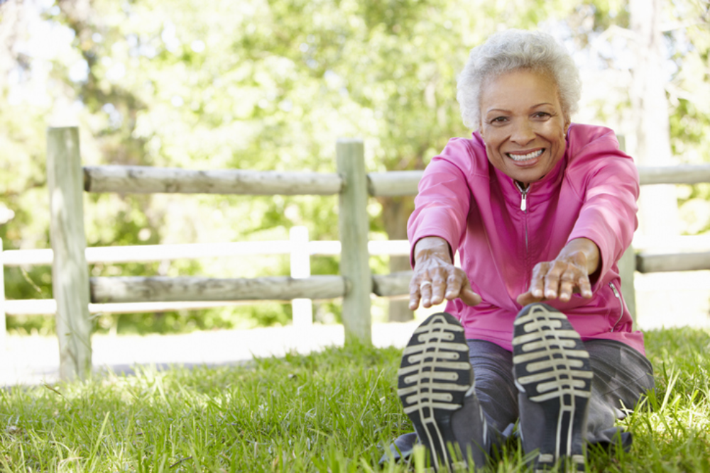 A patient laying in the grass smiling at the camera while she stretches reaching her toes